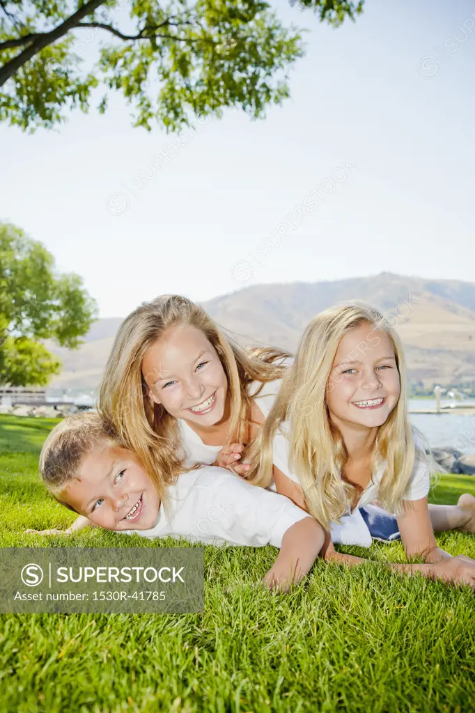 Three young children playing in lakeside park,