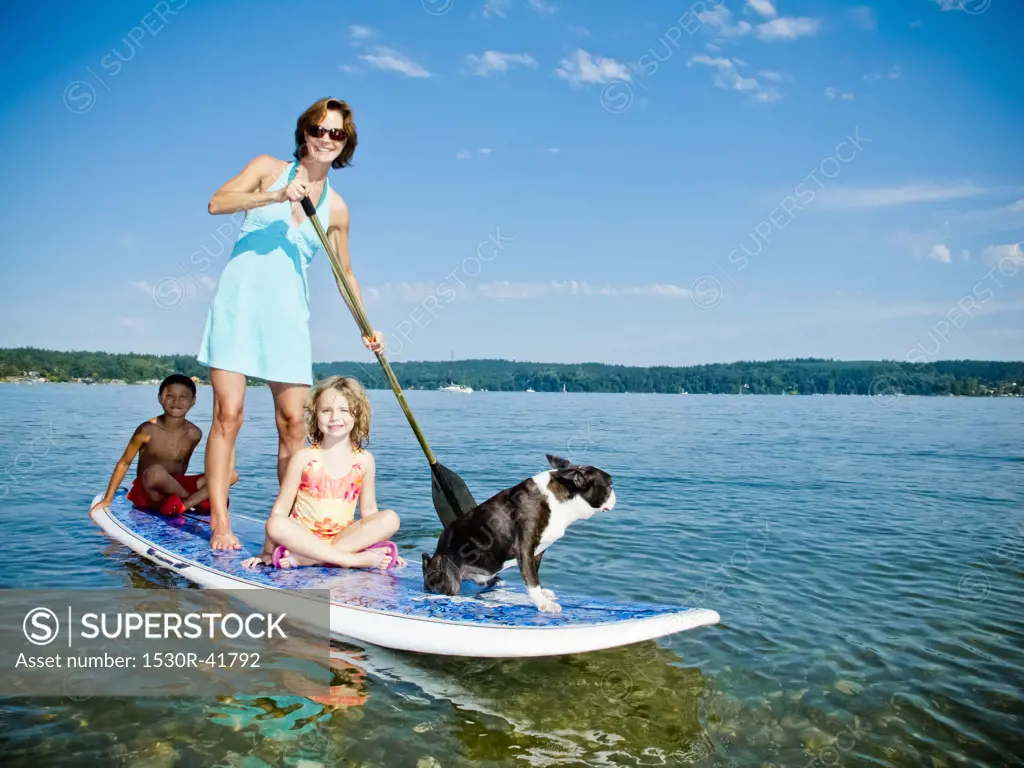 Woman on paddle board with kids and dog,