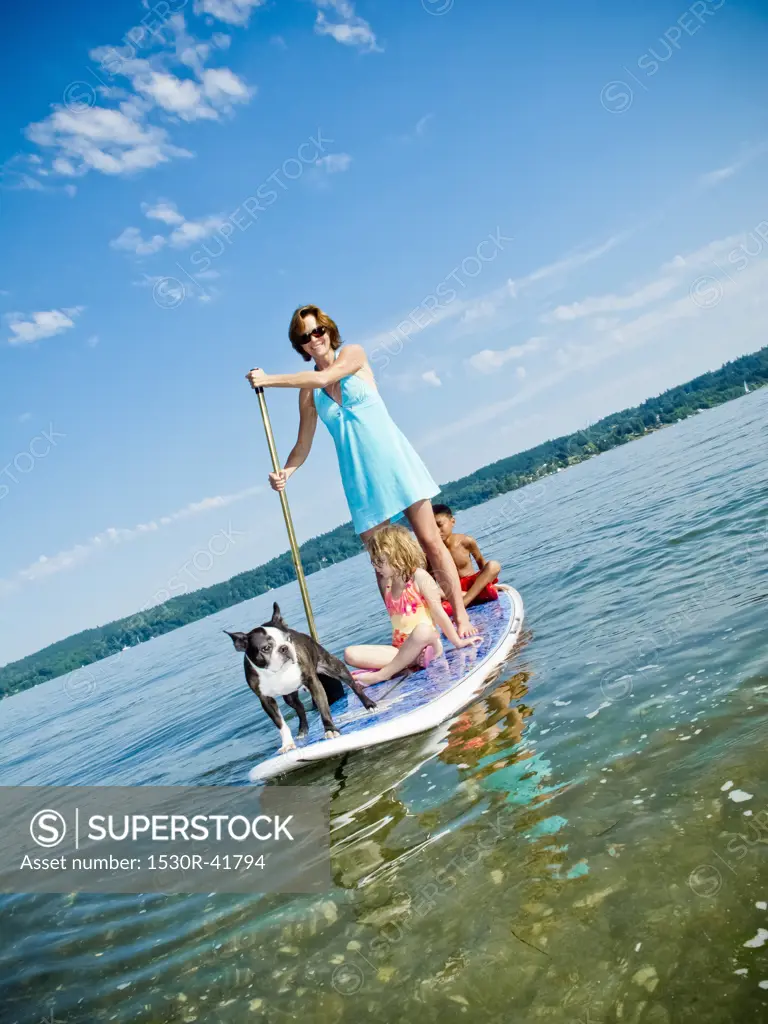 Woman on paddle board with kids and dog,