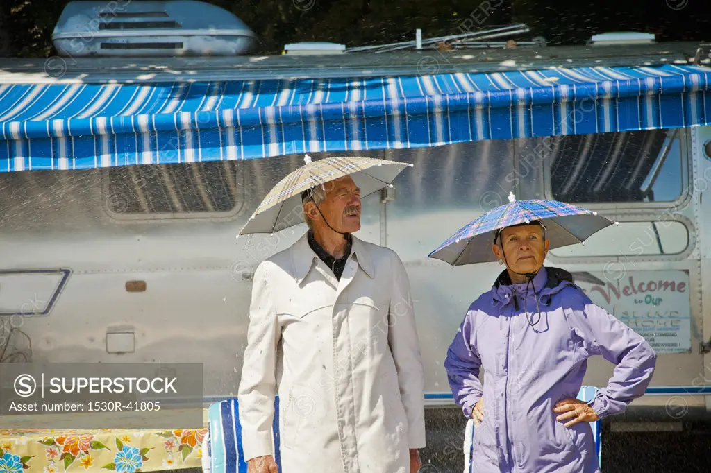 Senior couple in rain hats near airstream camper,