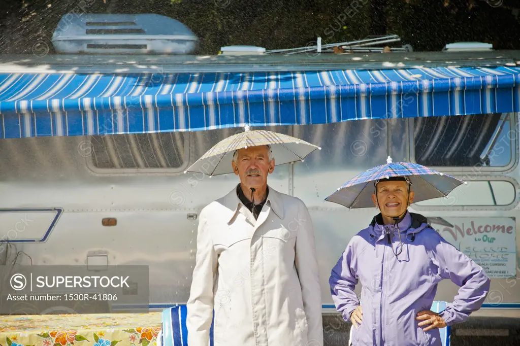 Senior couple in rain hats near airstream camper,