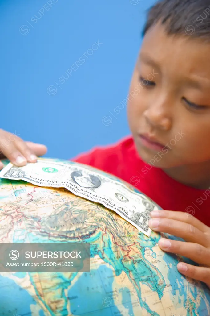 Boy placing dollar bill on globe,