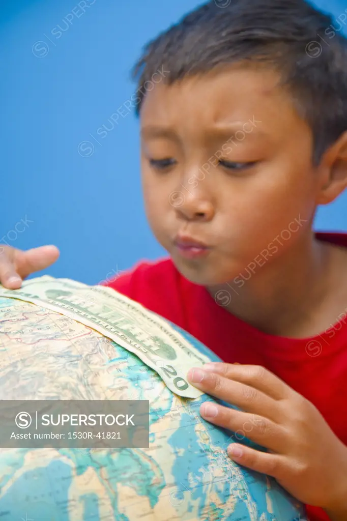 Boy placing 20 dollar bill on globe,