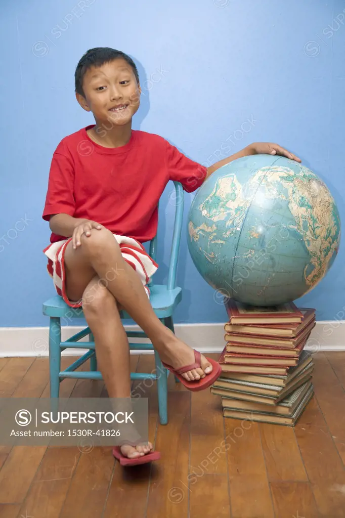 Boy seated next to globe resting on stack of books,
