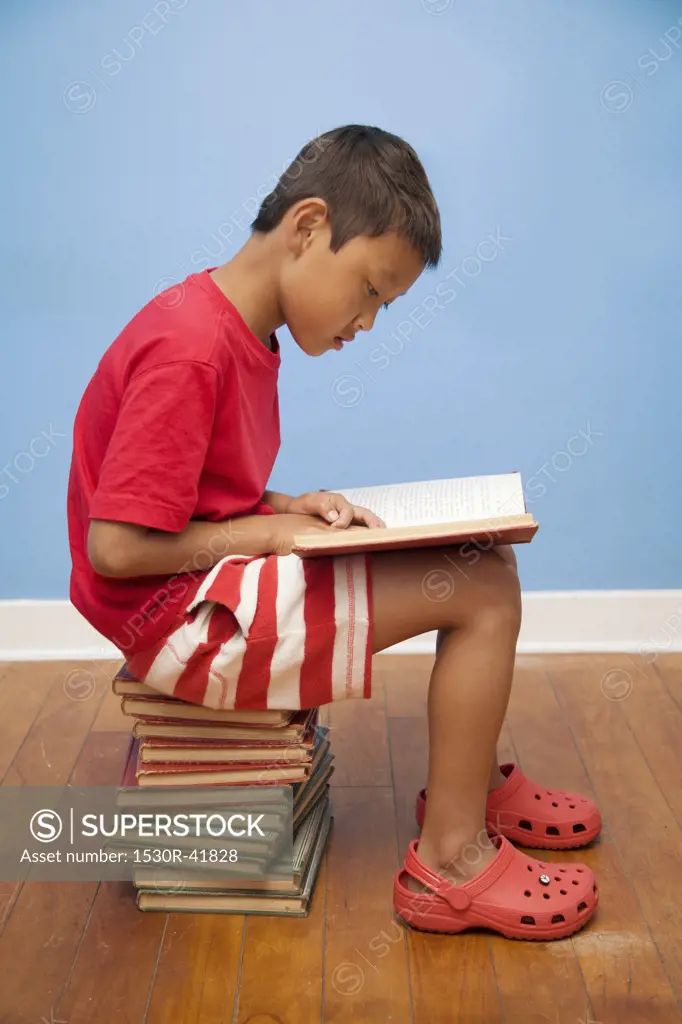 Boy reading while seated on stack of books,