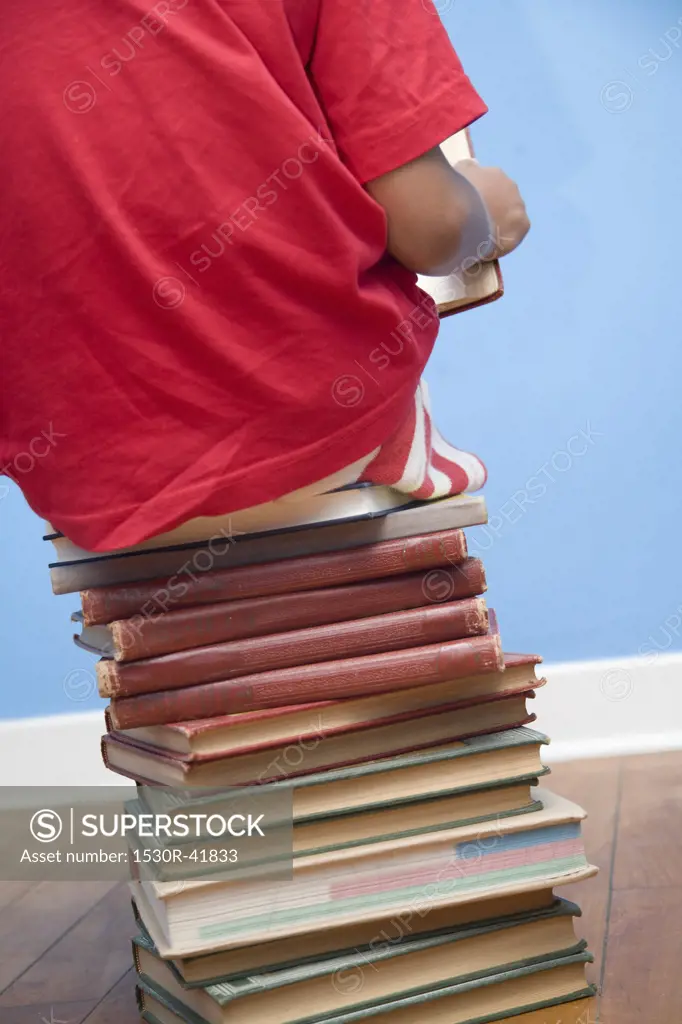 Rear view of boy sitting on stack of books,