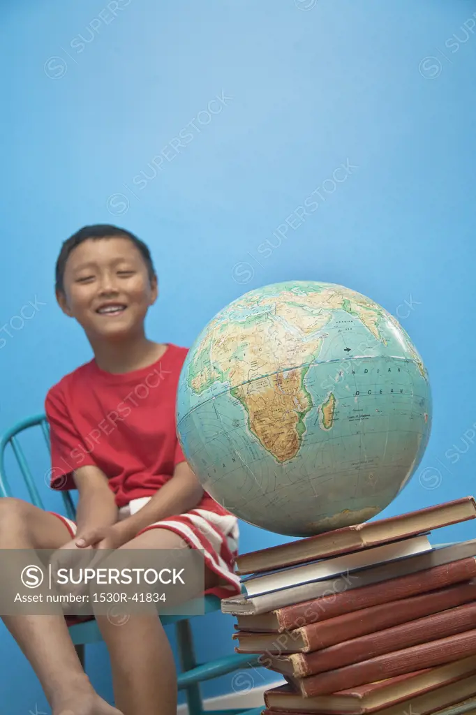 Boy seated near globe on top of books,