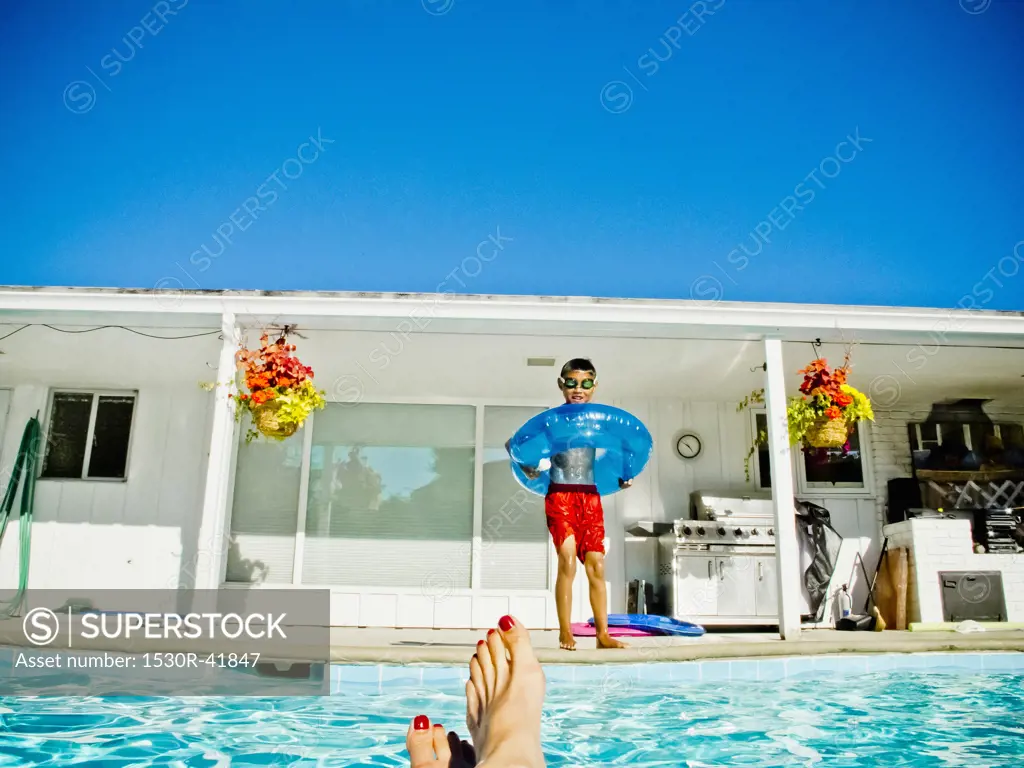 Boy in floaty standing next to pool,