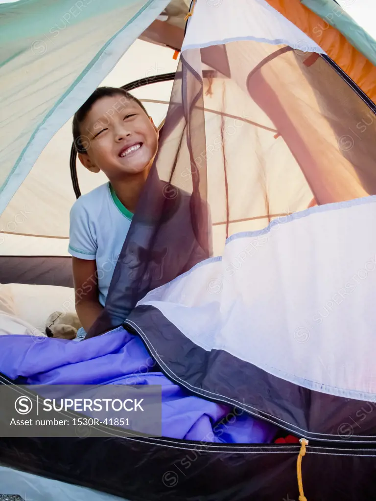 Young boy peeking out from tent on beach at sunrise,