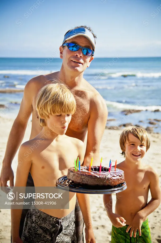 Man holding birthday cake on beach with two boys