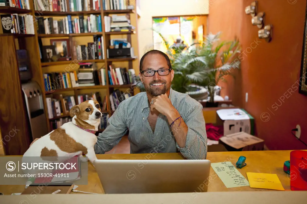 Man seated at home office with dog on desk