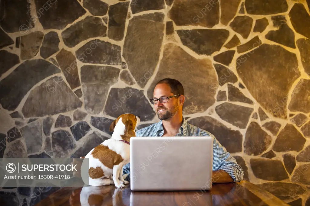 Man seated at long table with laptop and dog