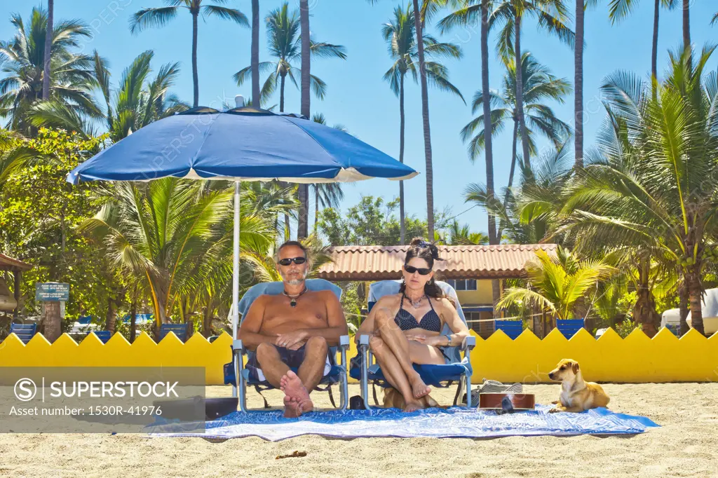 Grumpy man and woman on beach chairs under umbrella,  Sayulita, Mexico