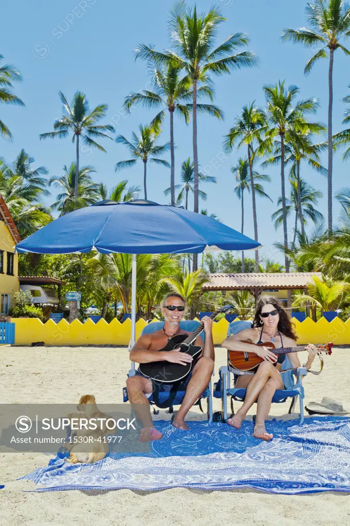 Happy man and woman in beach chairs with guitars and dogs,  Sayulita, Mexico