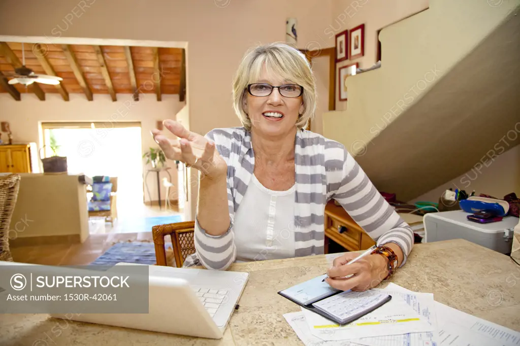 Woman working at home office with computer and bills