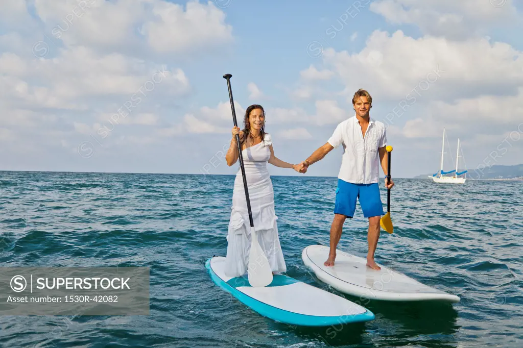 Dressed up man and woman riding paddle boards