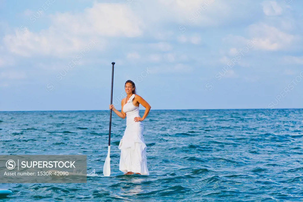 Woman in white dress riding paddle board