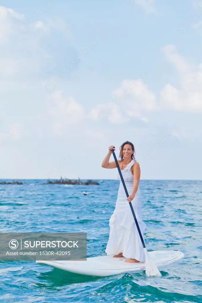Woman in white dress riding paddle board