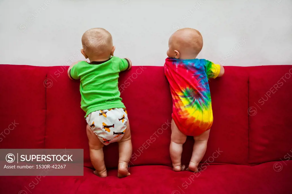 Two babies standing on red sofa