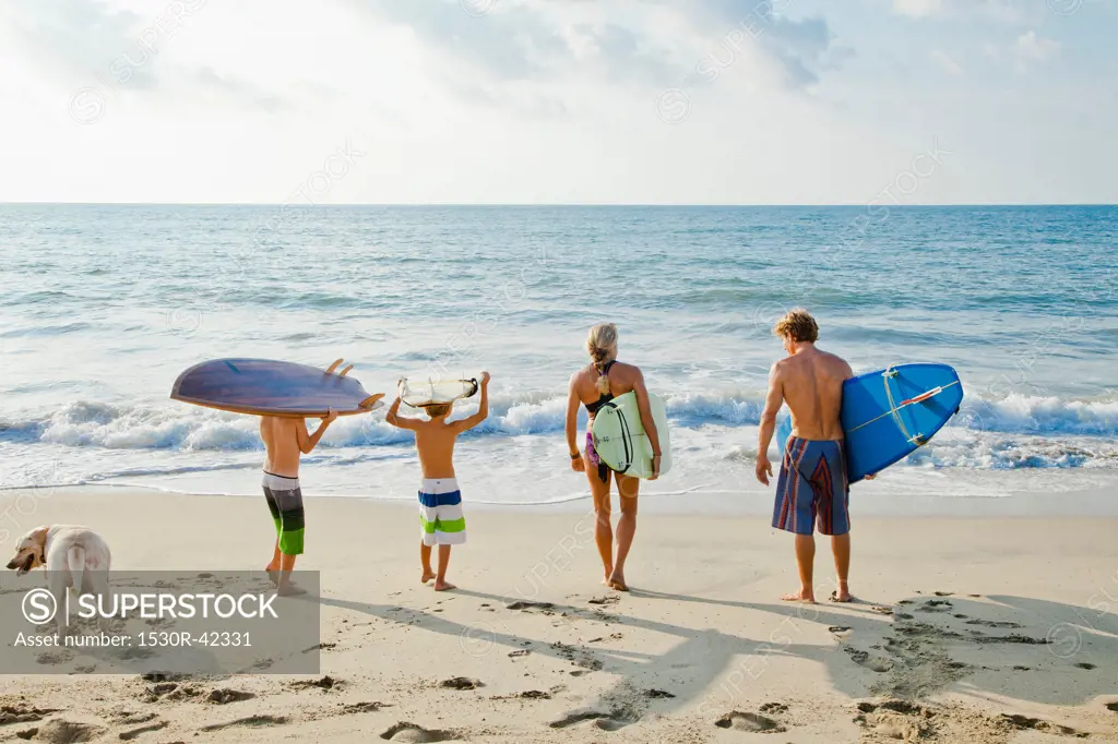 Family on beach holding surfboards