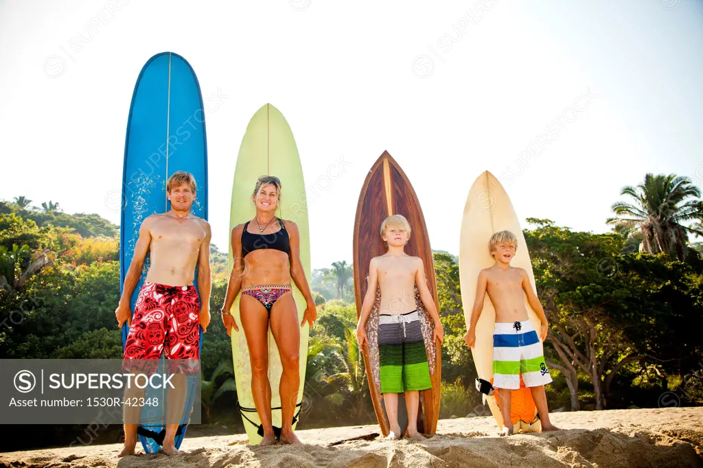 Family of four standing in front of surfboards