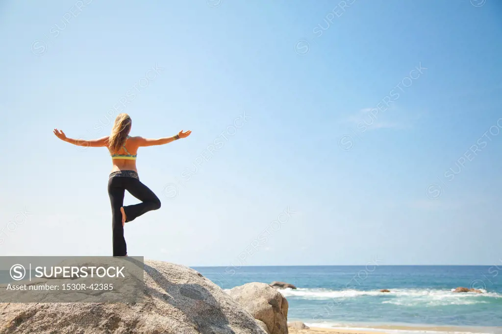 Young woman in yoga pose on rock by ocean