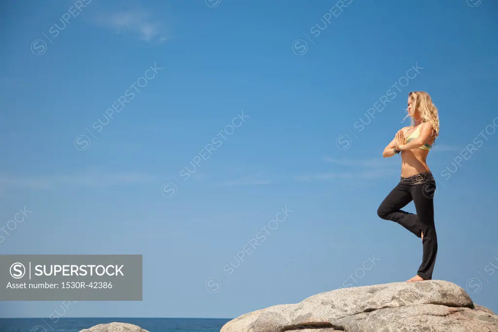 Young woman in yoga pose on rock by ocean