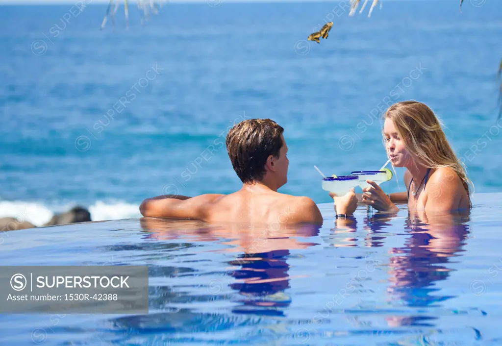 Young couple with cocktails in infinity pool