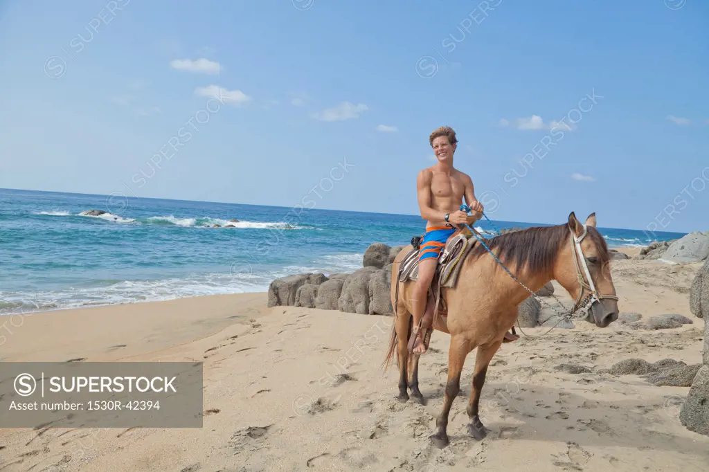Young man riding horse on beach