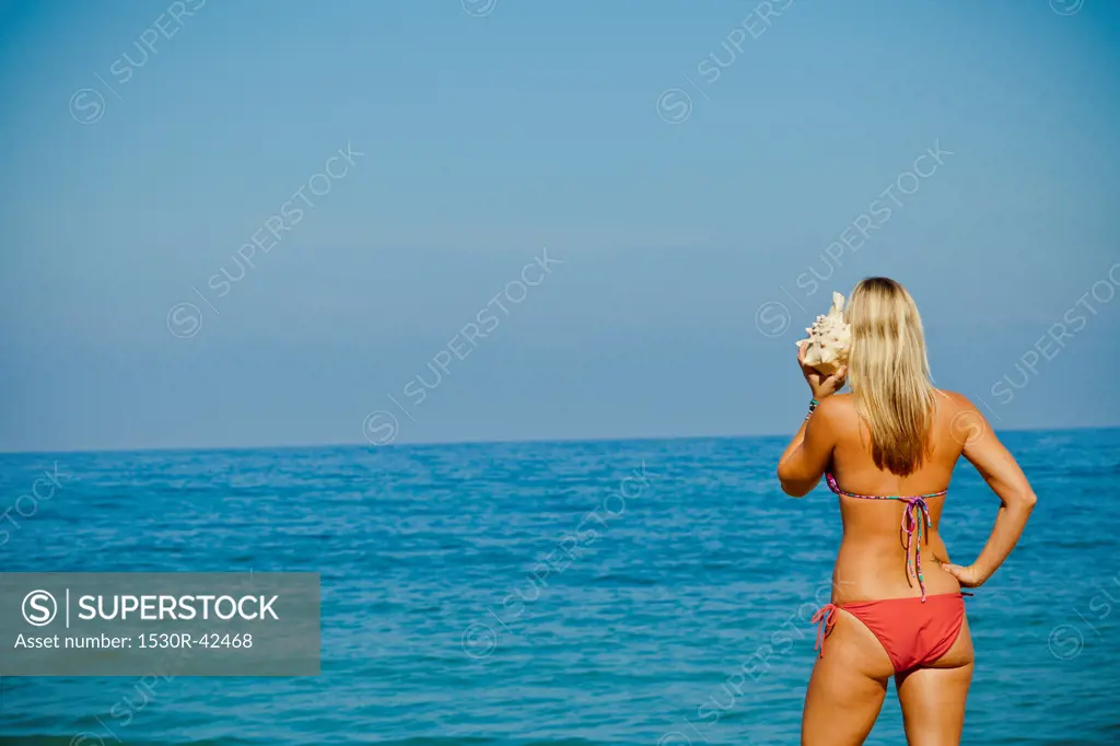 Woman on beach listening to large seashell