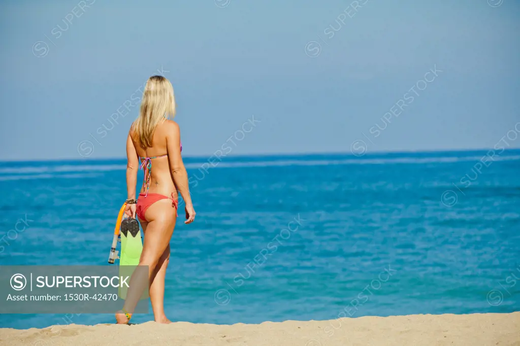 Woman walking on beach carrying swim fins