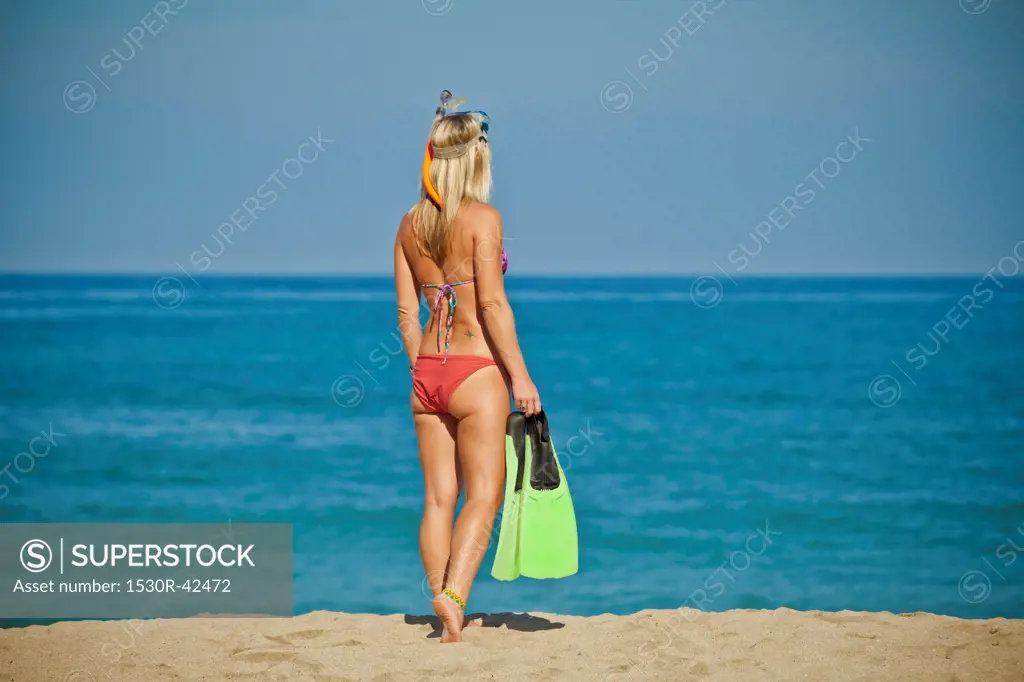 Woman walking on beach carrying swim fins