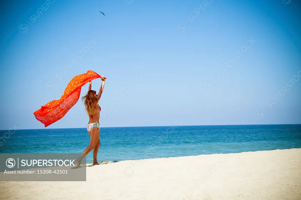 Woman running on beach holding sarong