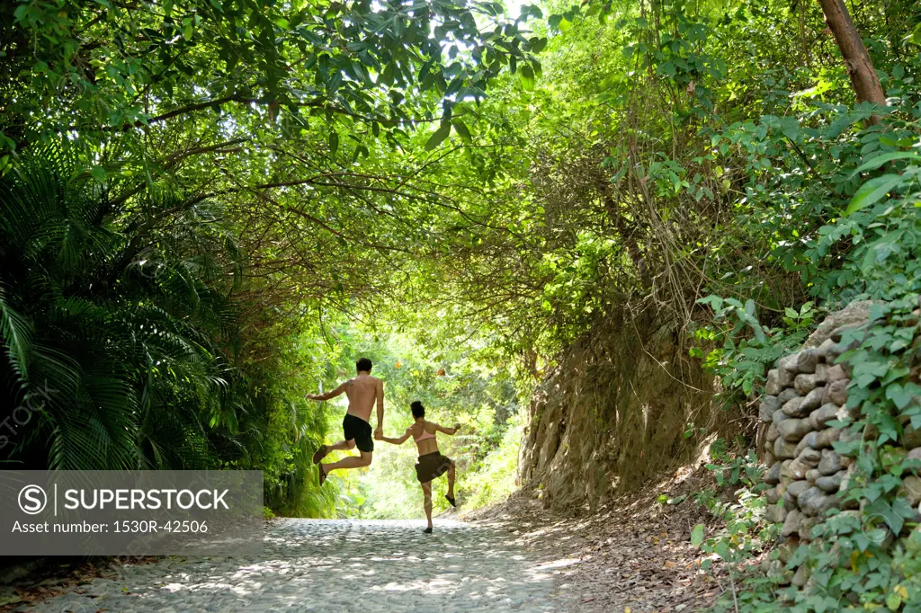 Couple jumping in air on tree arched path