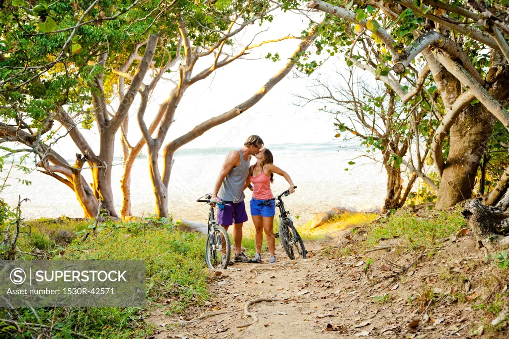 Couple riding bicycles on path to beach