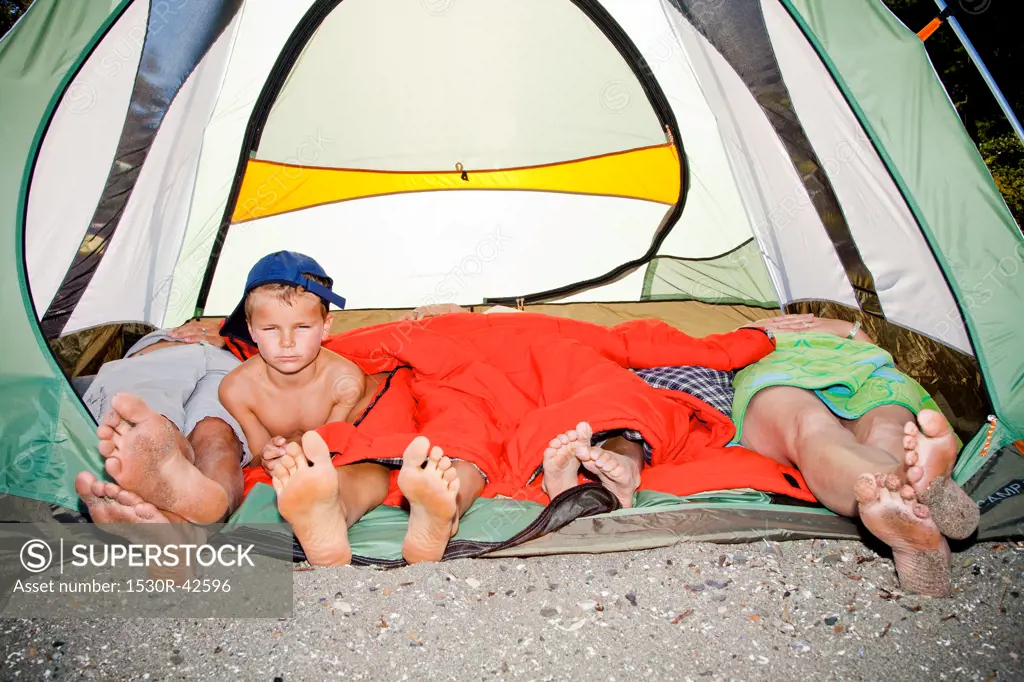 Young boy's face and pairs of feet poking out of tent