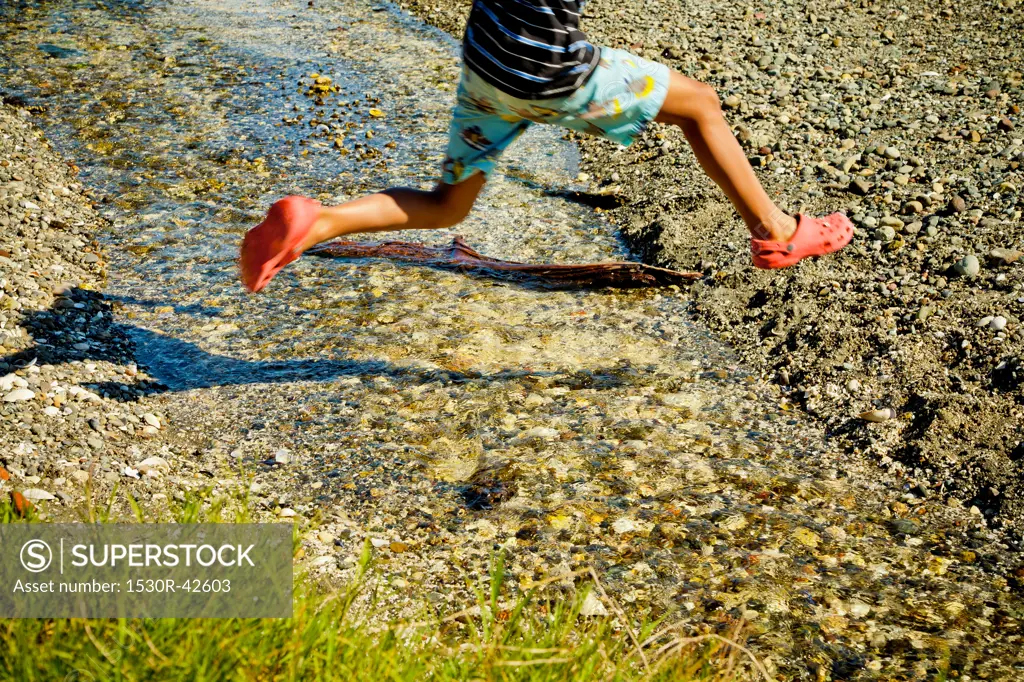 Young boy jumping over creek on beach