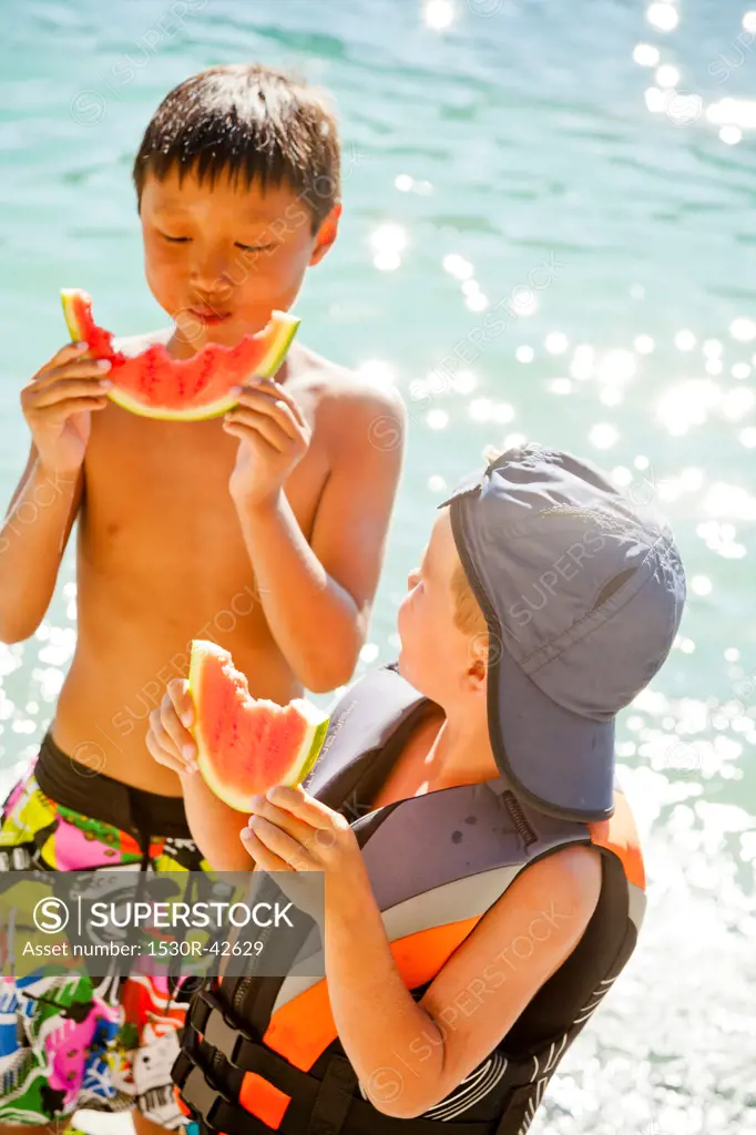 Young boys eating watermelon by lake