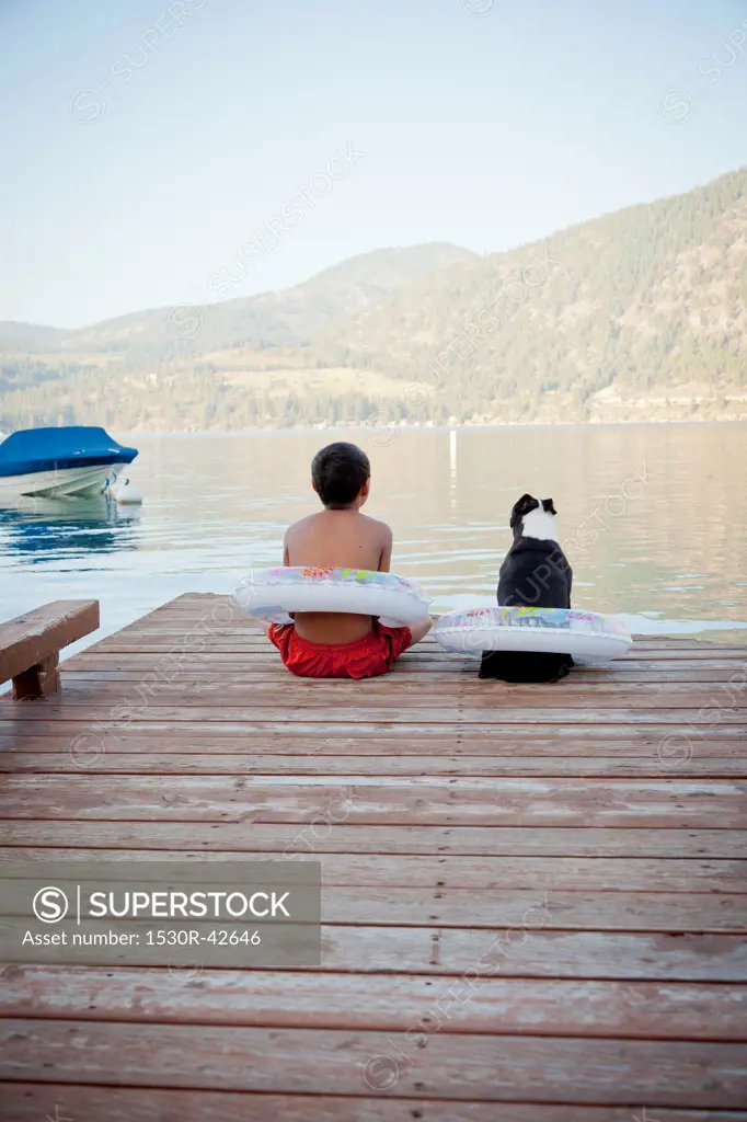 Young boy and dog wearing float rings on dock