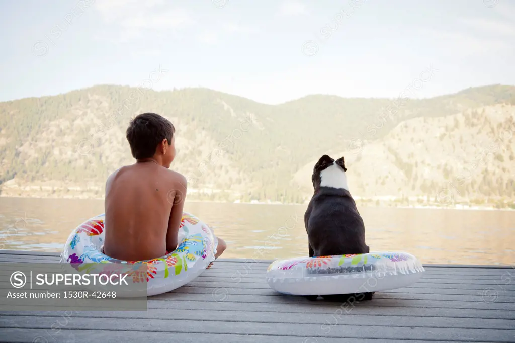 Young boy and dog wearing float rings on dock