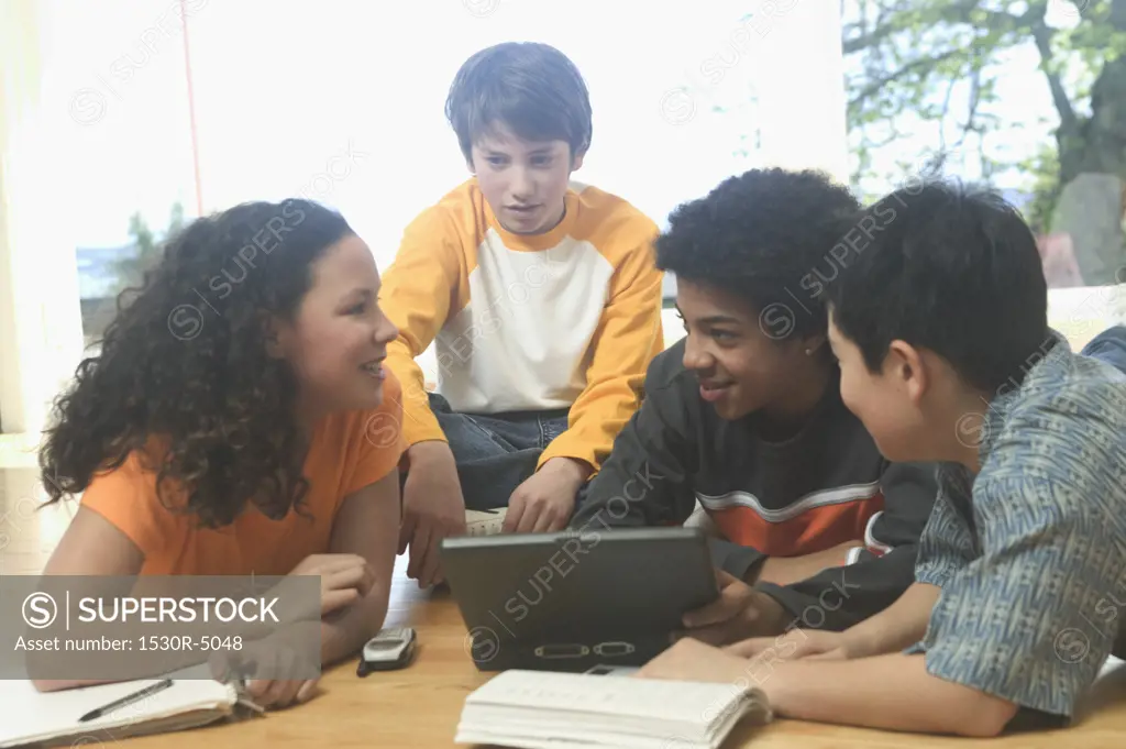 Four teenage kids working on a laptop and school books.  