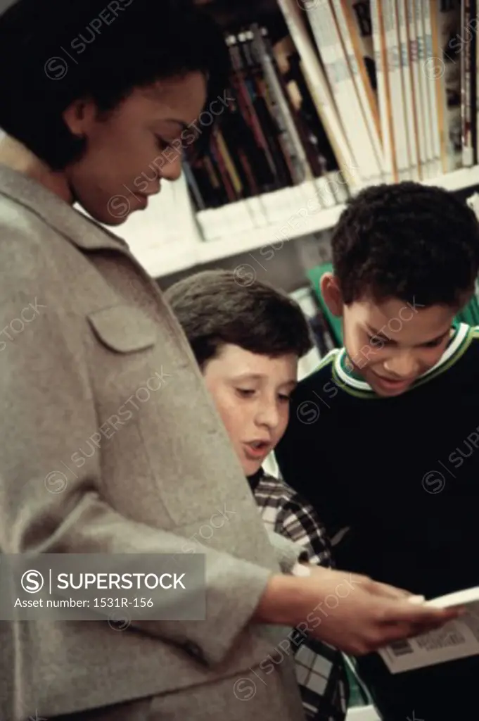 Female teacher reading a book with two students