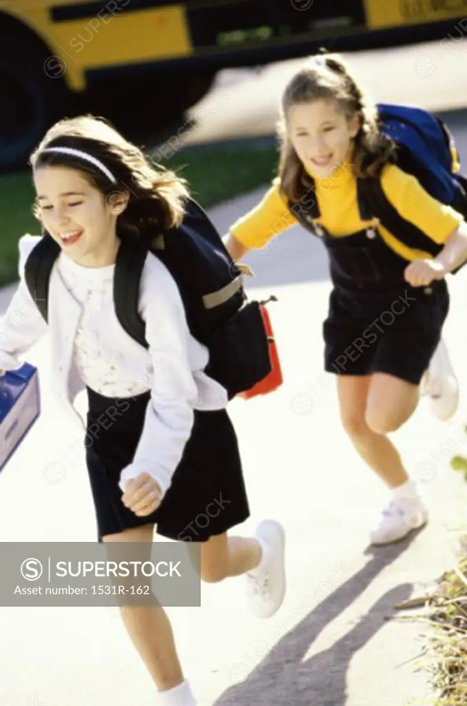 Two girls running with school bags on their backs
