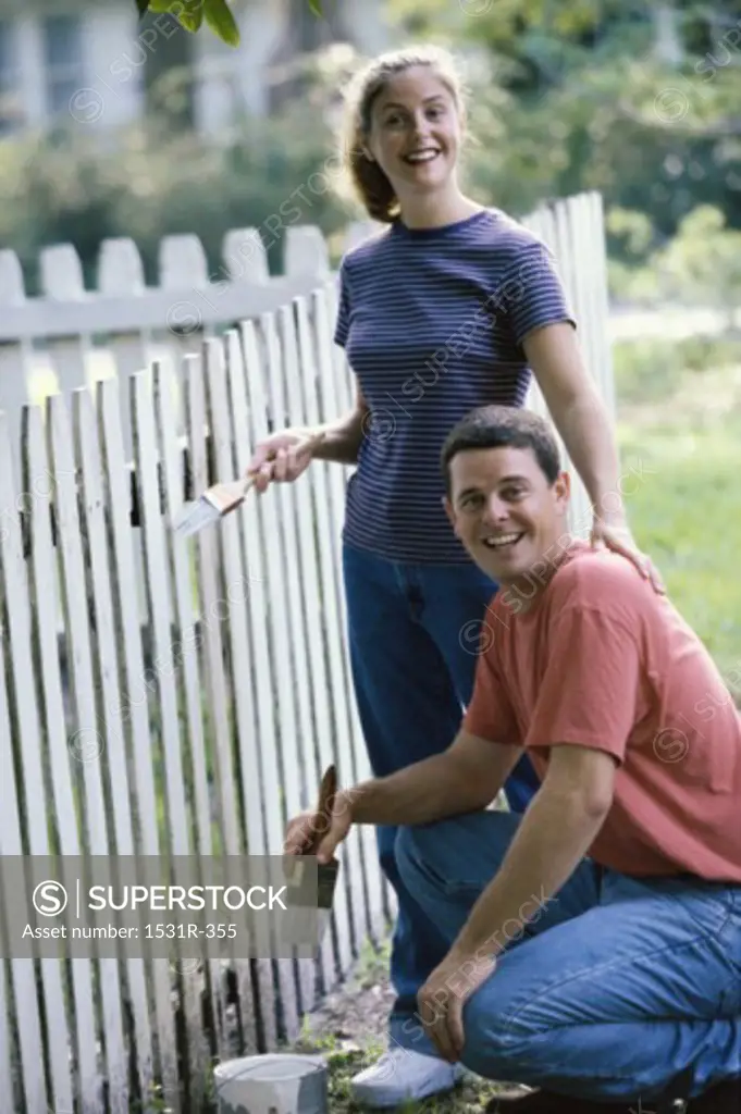Portrait of a young couple painting a fence