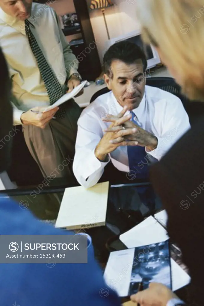 Businessman sitting with business executives standing around him