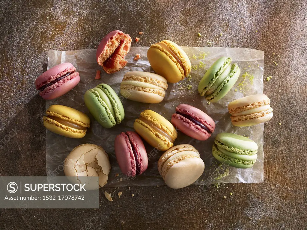 Different colorful macarons on paper against a wooden background