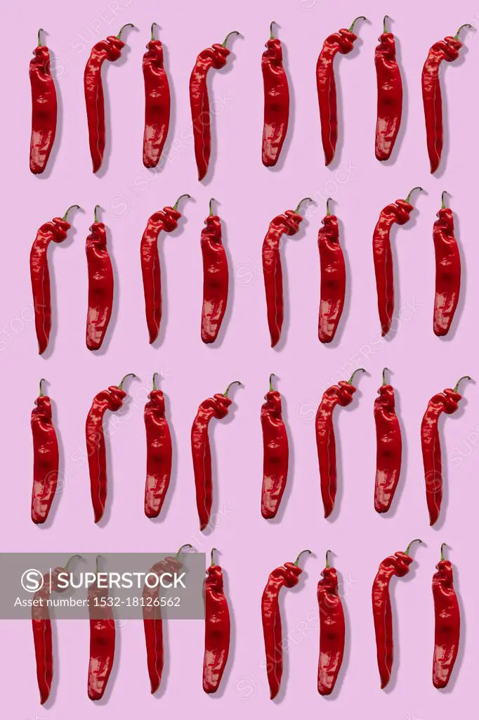 Four rows of red chillies on a pink background