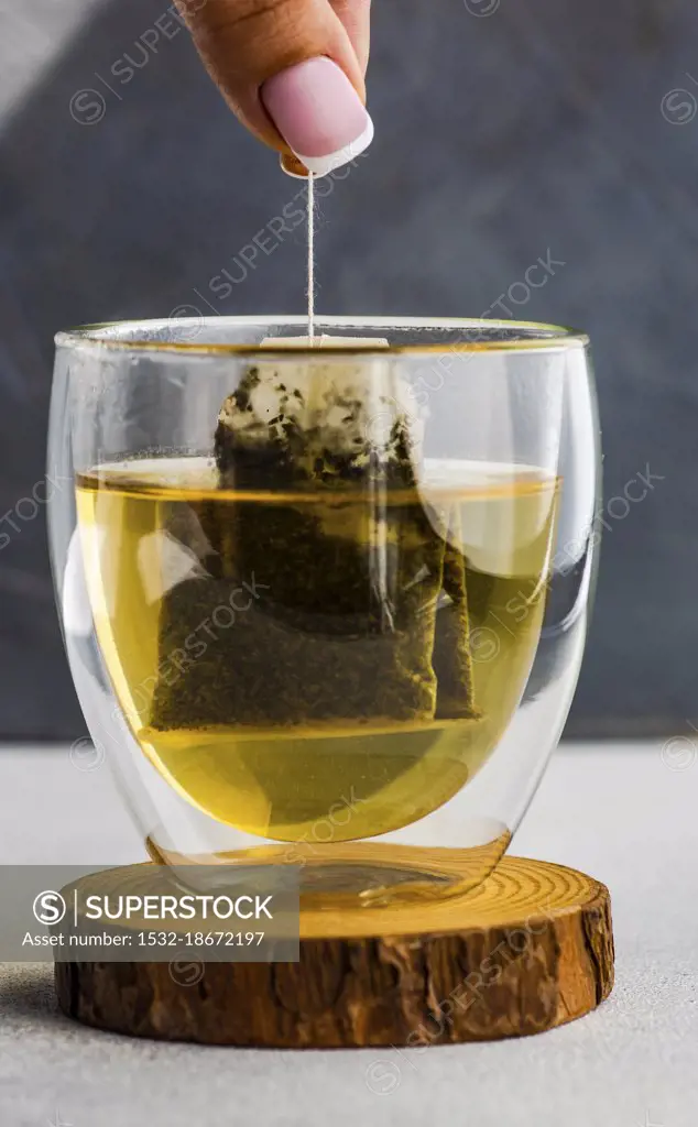 Woman hands hold of green tea bag in double glass cup
