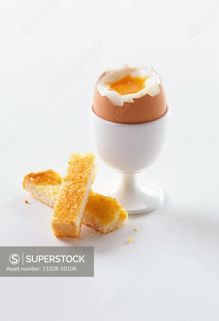 Breakfast egg in egg cup with top removed, pieces of toast