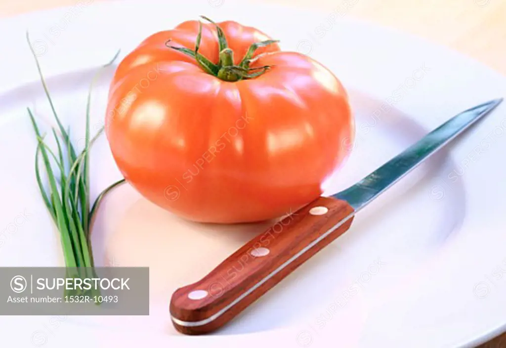 A tomato, chives and a knife on a plate